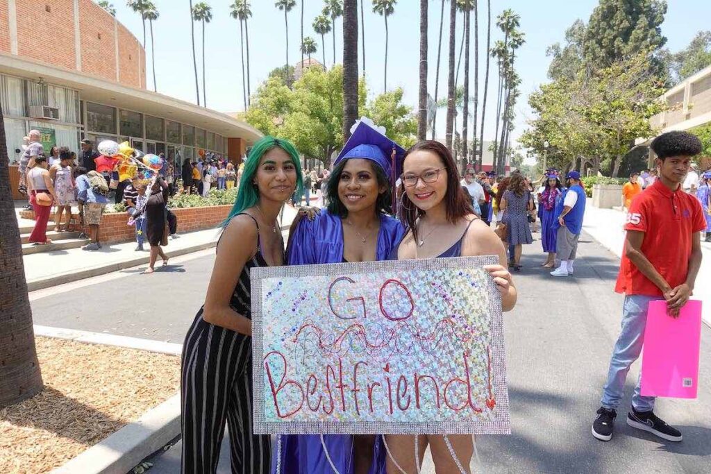 Gateway College and Career Academy graduate in cap and gown with friends holding sign