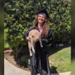 Empleada y ex alumna de GCCA lleva la toga y el birrete de graduación mientras sostiene un gato