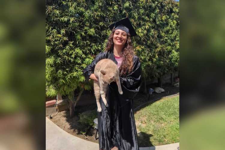 Empleada y ex alumna de GCCA lleva la toga y el birrete de graduación mientras sostiene un gato